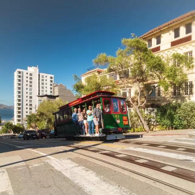 Die Seilbahn von Powell und Hyde fährt an einem sonnigen Tag mit lächelnden Menschen die Straße hinauf.